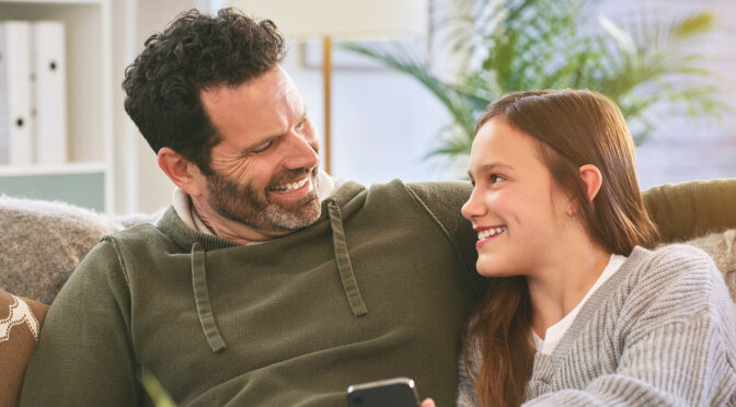 Family, happy and cellphone on couch for streaming videos, social media and notification. Man, teenage girl and technology in living room for connection, home and online for scroll and information